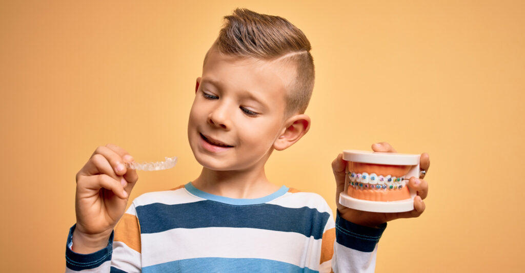 boy holding orthodontic denture with metal braces and invisible aligner
